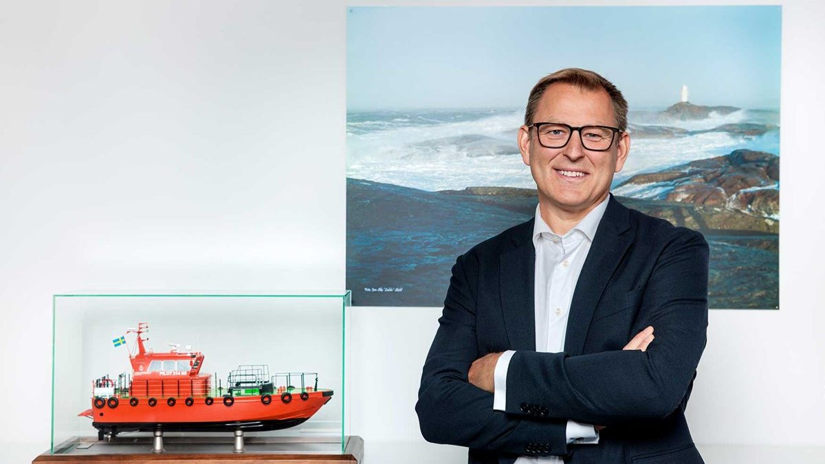 En medelåldersman med glasögon bredvid en monter med en modell av en orange lotsbåt.