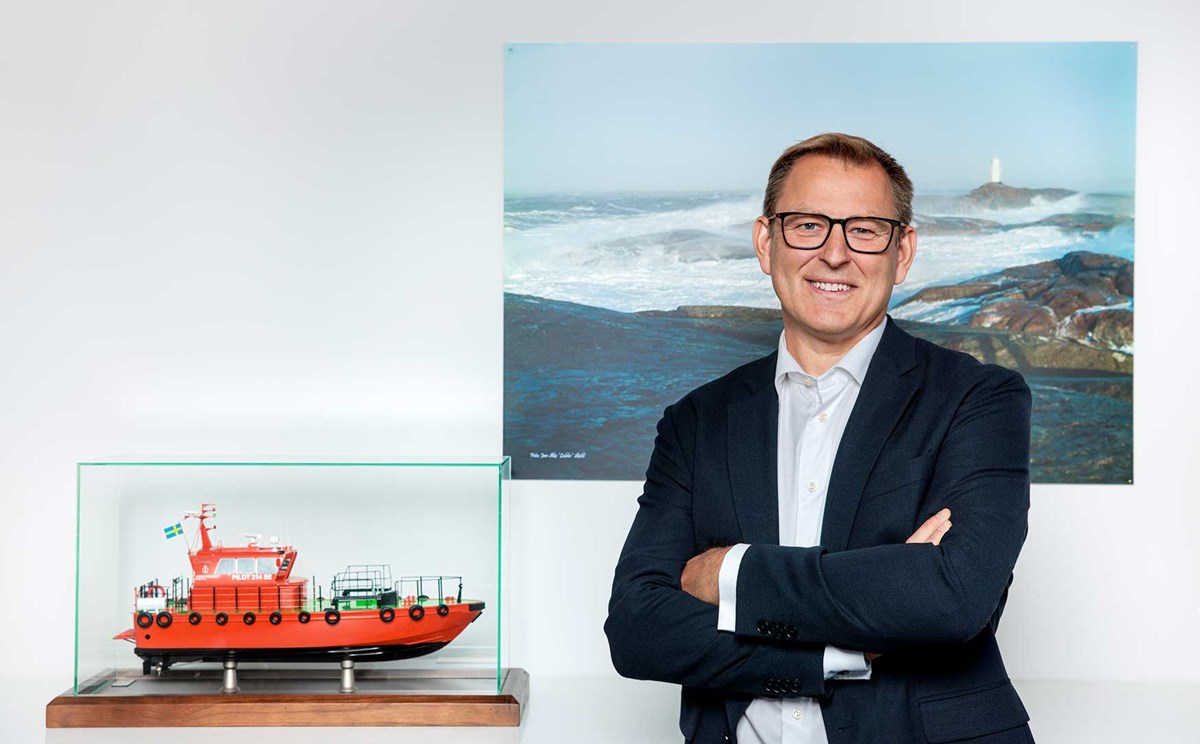 En medelåldersman med glasögon bredvid en monter med en modell av en orange lotsbåt.