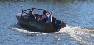Två personer i en liten trämotorbåt som kör bortåt.