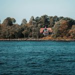 Bild på en liten ö med hus och flaggstång med svenska flaggan, i skärgården.