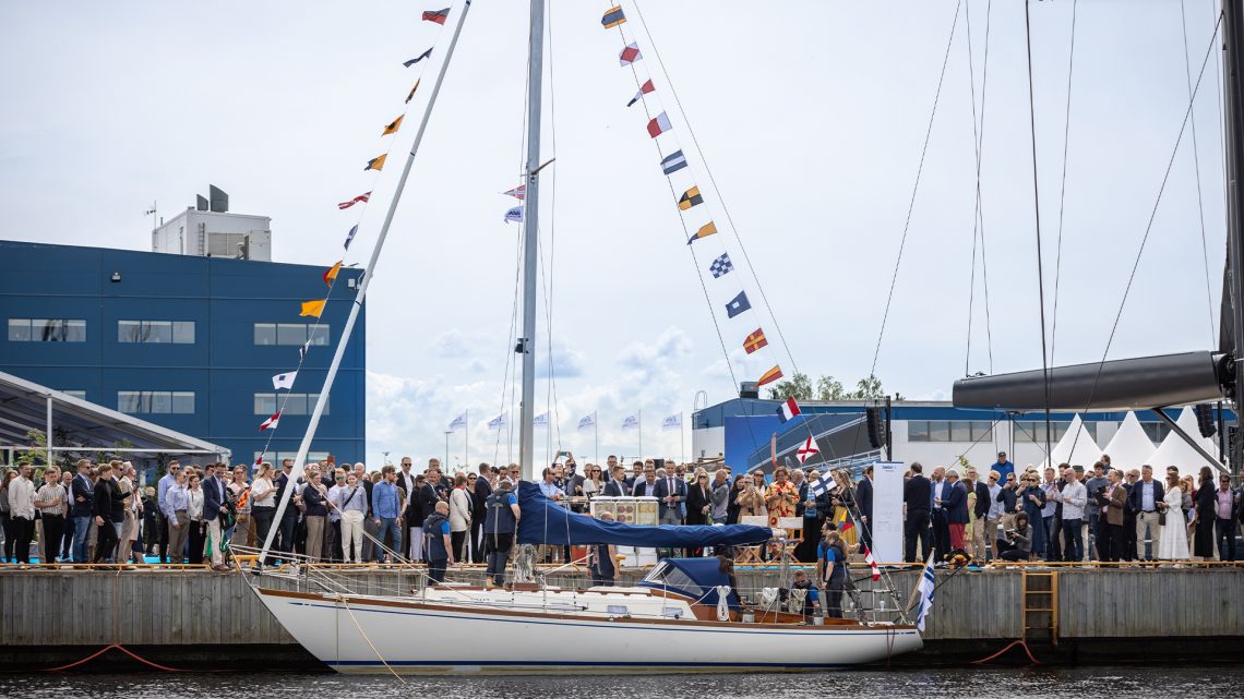 En äldre segelbåt med vitt skrov i hamn. Vimplar hänger på för och akterstag.