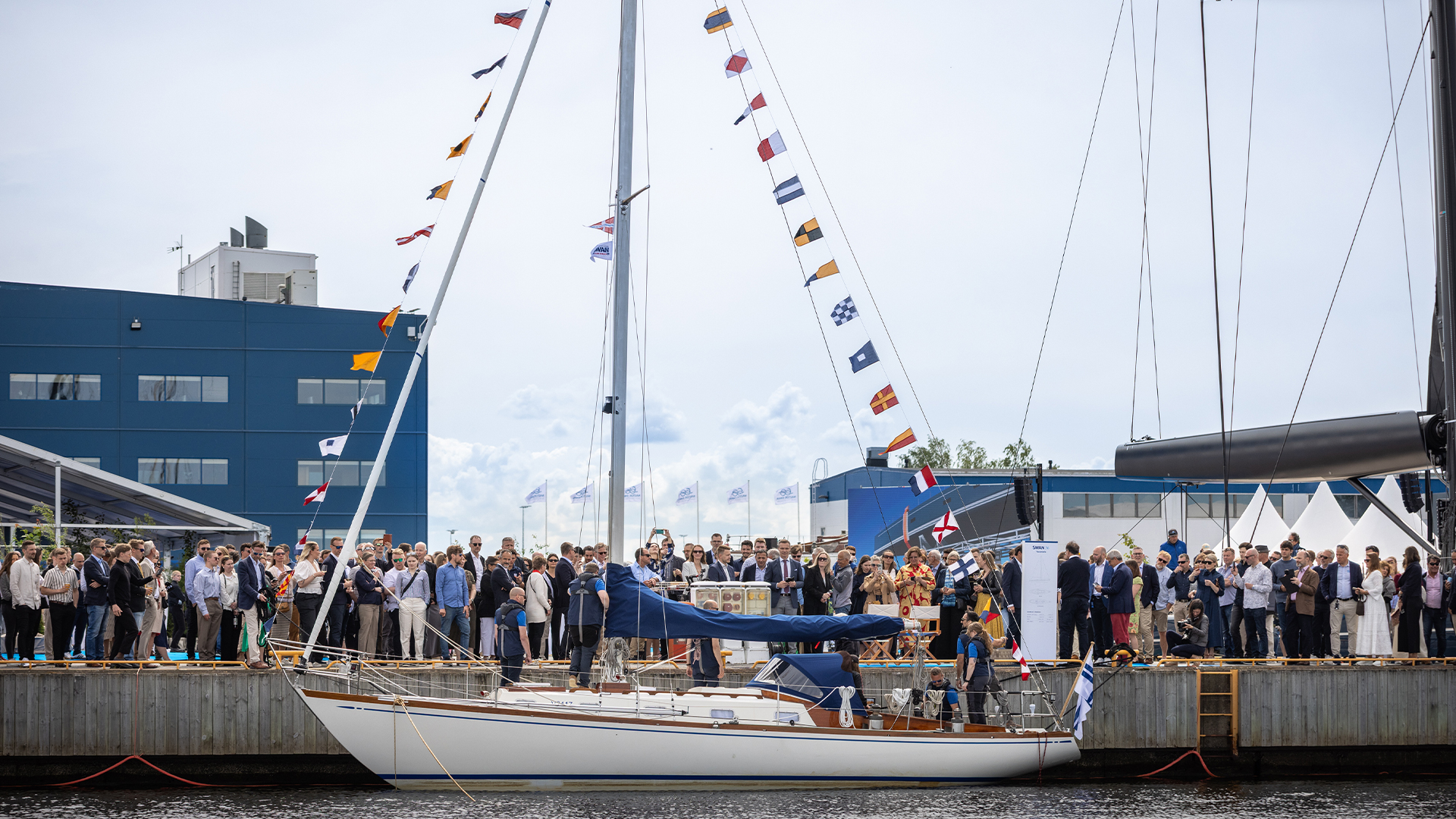 En äldre segelbåt med vitt skrov i hamn. Vimplar hänger på för och akterstag.