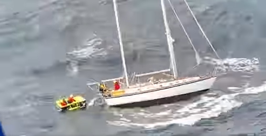 Dåligt upplöst bild av en segelbåt ute till havs med en räddningsflotte bakom, som det sitter två personer i.