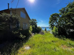 Ett gult bostadshus, ganska nedgånget. Vid sidan av huset ser man ut över havsviken.