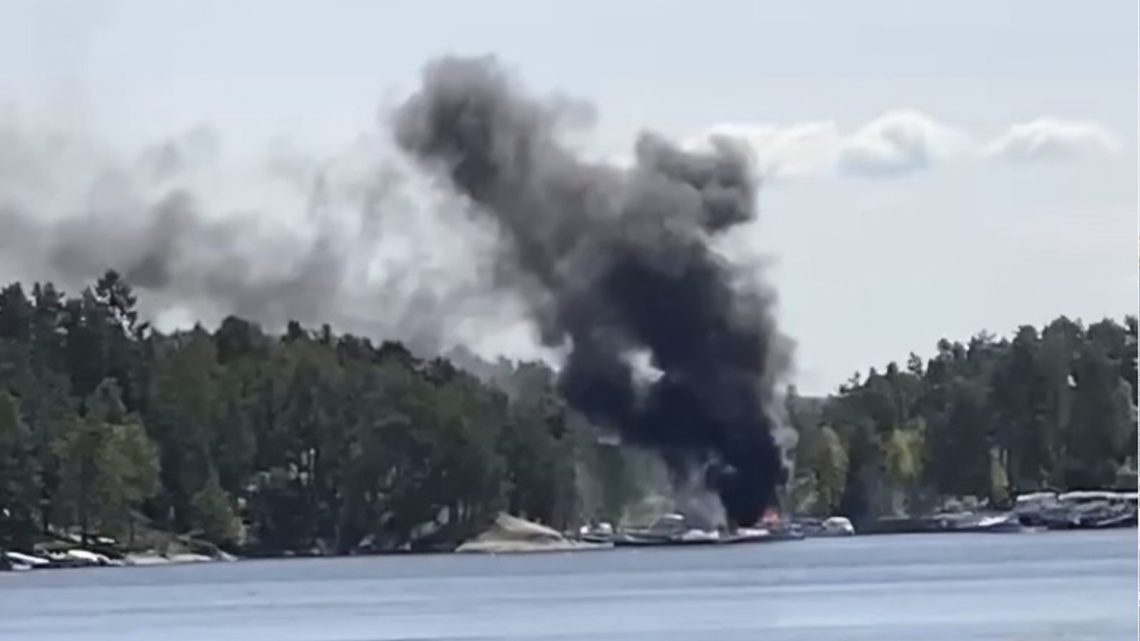Bild från avstånd på en småbåtshamn, där det stiger en stor rökpelare från några båtar.