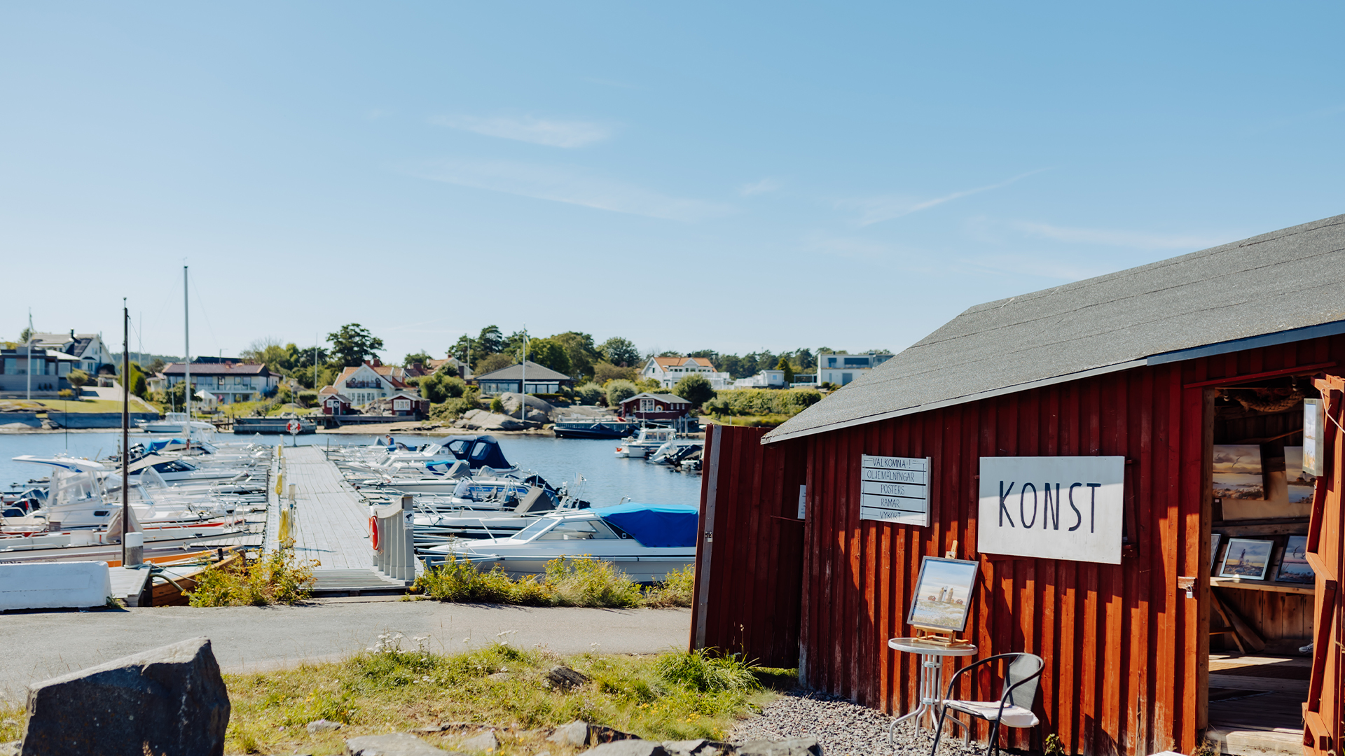 Småbåtshamn på västkusten. Till höger en faluröd sjöbod. På en skylt står det "konst".