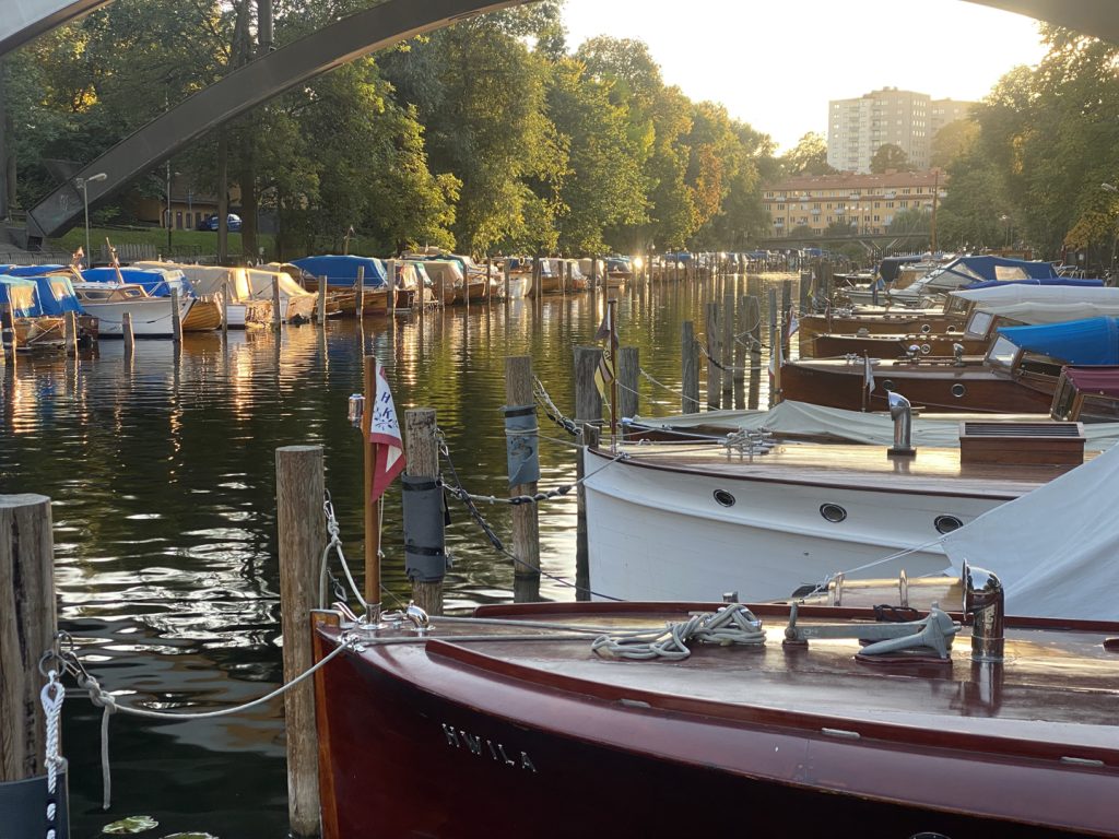 Ett antal träbåtar på ömse sidor om en kanal i morgonljus.