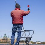 En man står i fören på en segelbåt, som används som startbåt i en kappsegling.
