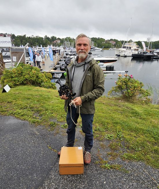 En man med sextant i handen står framför en småbåtshamn.