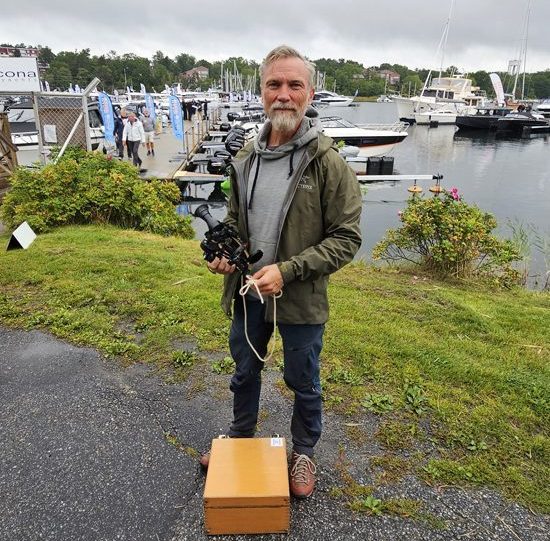 En man med sextant i handen står framför en småbåtshamn.