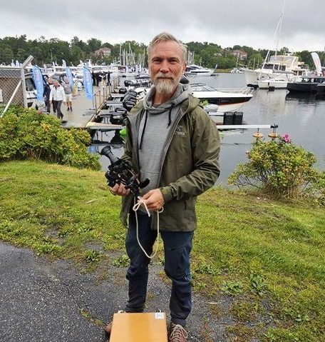 En man med sextant i handen står framför en småbåtshamn.