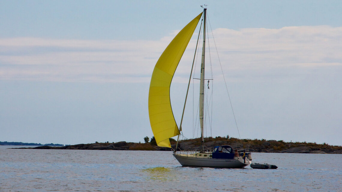 En segelbåt med gult försegel som seglar i skärgård.