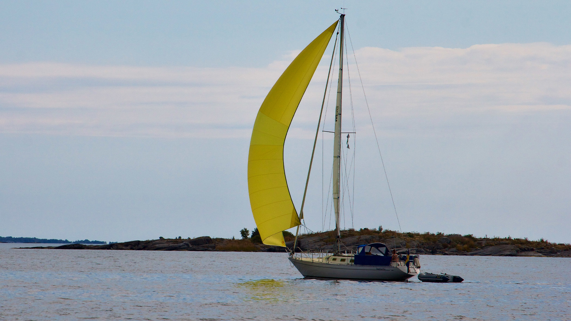 En segelbåt med gult försegel som seglar i skärgård.