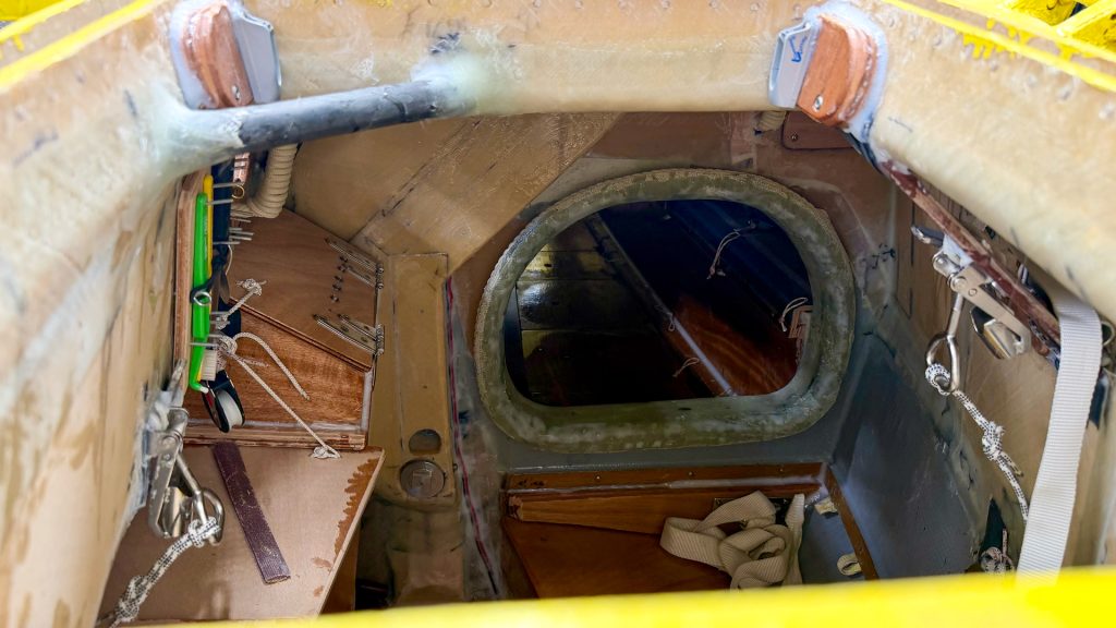 Insidan av en väldigt liten segelbåt. Litet utrymme och spartanskt inrett.